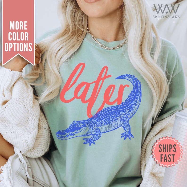 May include: A light blue t-shirt with a blue and white alligator graphic and the word "later" in red lettering.