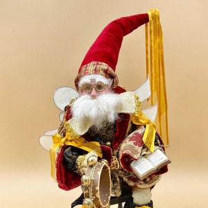 May include: A red and gold Christmas elf figurine with a white beard, wearing glasses and holding a tambourine and a book. The elf is sitting on a small wooden chair with gold accents.
