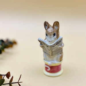 May include: A brown and white ceramic figurine of a mouse reading a newspaper titled "The Gollar Gutter". The mouse is sitting on a red and yellow spool of thread.