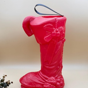 May include: A bright red Christmas stocking with a black handle. The stocking is decorated with a bow, berries, and a ribbon. The boot-shaped stocking is made of a shiny plastic material.