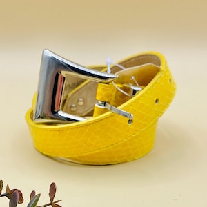 May include: A yellow leather belt with a silver buckle. The belt is folded in half and the buckle is visible.