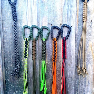 May include: Seven colorful paracord keychains with black metal clips. The keychains are made with different colored paracord and have a variety of patterns.