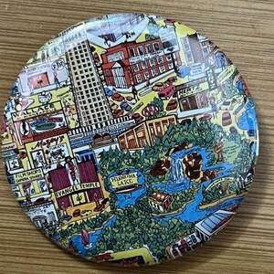 Pode incluir: Um botão redondo e colorido que apresenta um mapa detalhado de Minneapolis, Minnesota. O mapa inclui pontos de referência como o horizonte da cidade, a cadeia de lagos e a Universidade de Minnesota.