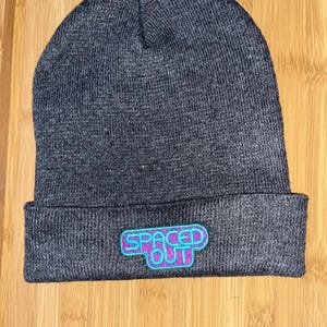 May include: Gray knit beanie with a purple and teal "Spaced Out" embroidered patch.