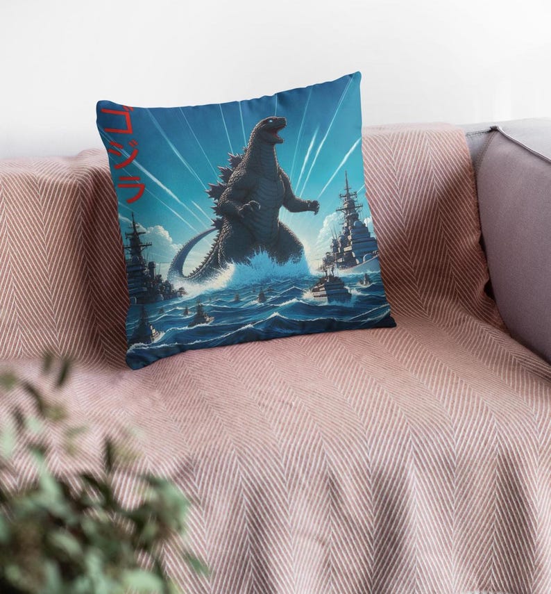May include: A blue and white throw pillow with a black and white illustration of Godzilla standing in the ocean with ships in the background. The text "ゴジラ" is written in red on the pillow.