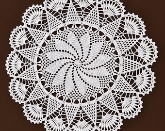 May include: A round white crochet doily featuring a central spiral pattern of radiating petals, surrounded by a complex geometric mesh and a wide outer border composed of repeating fan-shaped motifs with scalloped edges.