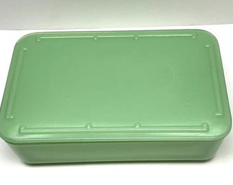 以下が含まれることがあります： 淡い緑色のガラス製長方形保存容器と、それに対応する蓋。蓋には縁取りのデザインが施されており、四隅と側面に小さな円形のアクセントがあるため、表面は構造的で均一な外観になっています。