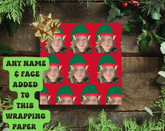 Puede incluir: Papel de regalo rojo con un patrón repetido de la cara de una persona con un gorro de elfo. Un lazo dorado está encima. El texto en un letrero verde dice "ANY NAME & FACE ADDED TO THIS WRAPPING PAPER."