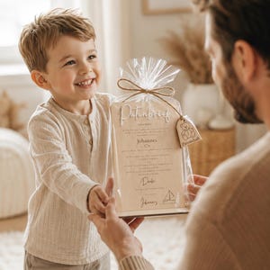 May include: A rectangular wooden plaque with the text Patenbrief and Johannes printed on it, enclosed in a clear plastic bag tied with twine. A small wooden tag shaped like a teddy bear with the word Patenschaft is attached to the twine.