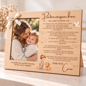 May include: A rectangular wooden photo frame featuring a light-colored ribbon bow on the left side. The frame displays a photograph of an adult and a child, with German text engraved on the right side and bottom, including a small illustration of a lion.