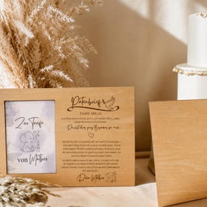 May include: A rectangular wooden frame featuring a left-side photo insert with a blue elephant illustration and the text Zur Taufe von Mathes. The right side displays engraved German text titled Patenbrief with a dove and heart icon.