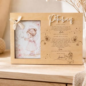 May include: A rectangular wooden frame featuring a light-colored wood finish. The left side holds a picture of an angel girl with a dove, accented by a cream-colored ribbon. The right side displays the text Patenbrief and a German letter.