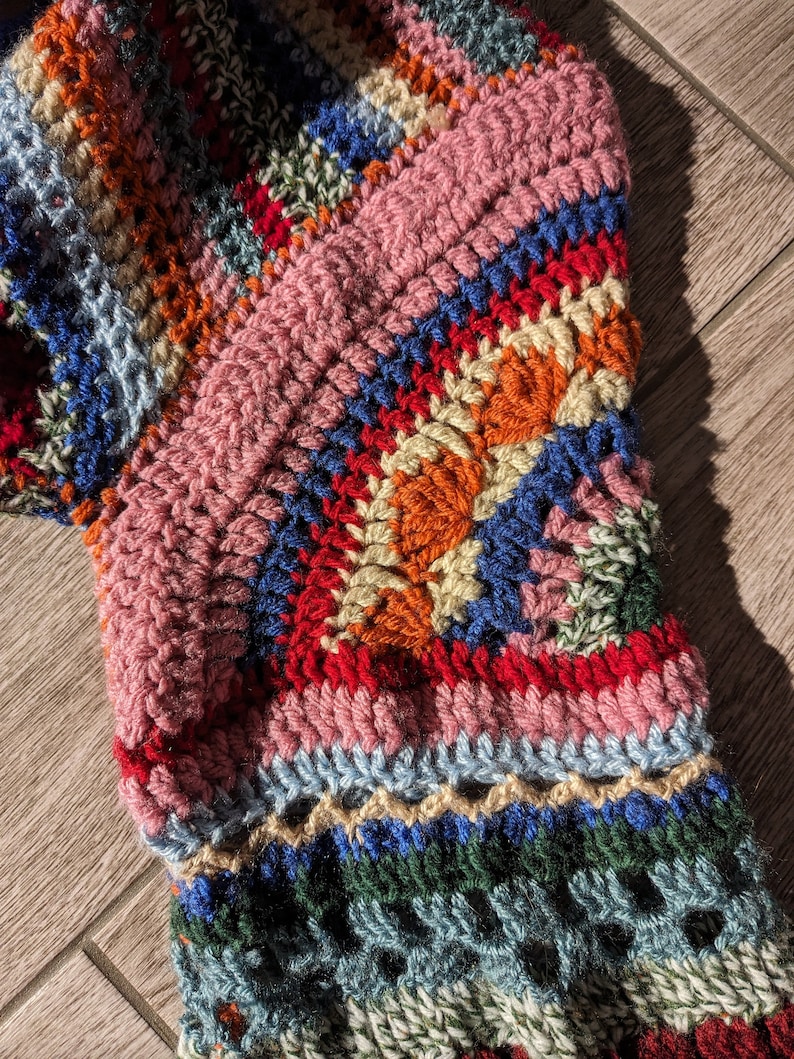 May include: Close-up of a colorful, handmade crochet item. The piece features a variety of colors including pink, blue, orange, red, and green. The texture is thick and the stitches are clearly visible, suggesting a cozy, handcrafted textile.
