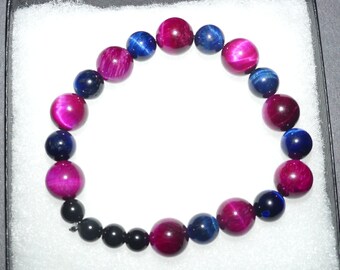 Puede incluir: Una pulsera de cuentas con cuentas redondas pulidas que alternan tonos vibrantes de magenta, azul intenso y negro sólido. Las cuentas están dispuestas en un patrón circular, mostrando una textura de superficie lisa y reflectante en cada cuenta.