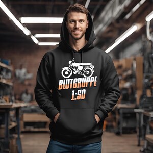 Op de afbeelding: Zwart hoodie met een witte afbeelding van een motorfiets en de tekst "Blutgruppe 1:50".
