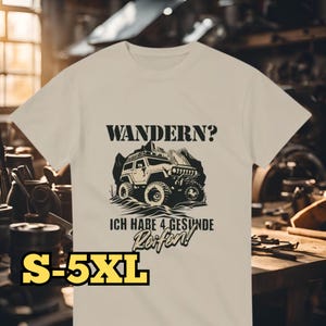 Può includere: Maglietta bianca con un'illustrazione in bianco e nero di una jeep con il testo "Wandern? Ich habe 4 gesunde Reifen!" e le taglie S-5XL stampate in basso.