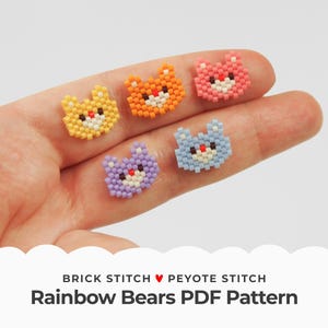 Puede incluir: Cinco pequeños abalorios de oso de colores arcoíris, hechos con punto de ladrillo y punto de peyote, se muestran en una mano. Los abalorios son de color naranja, amarillo, azul claro, morado y rosa.