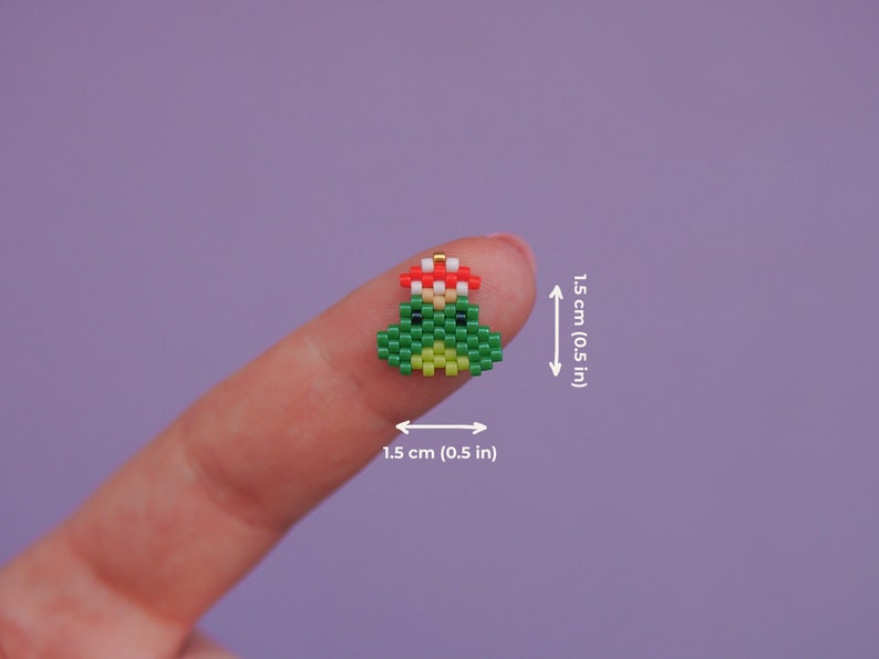 May include: A green frog with a red flower on its head, made of beads. The frog is about 0.5 inches tall.