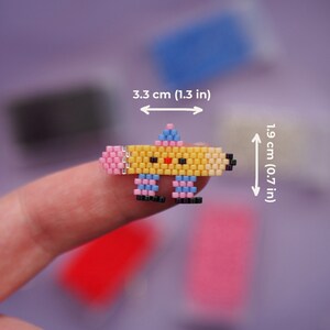 May include: A yellow, pink, and blue beaded pencil charm with a smiling face. The charm is 1.9 inches tall and 3.3 inches wide.