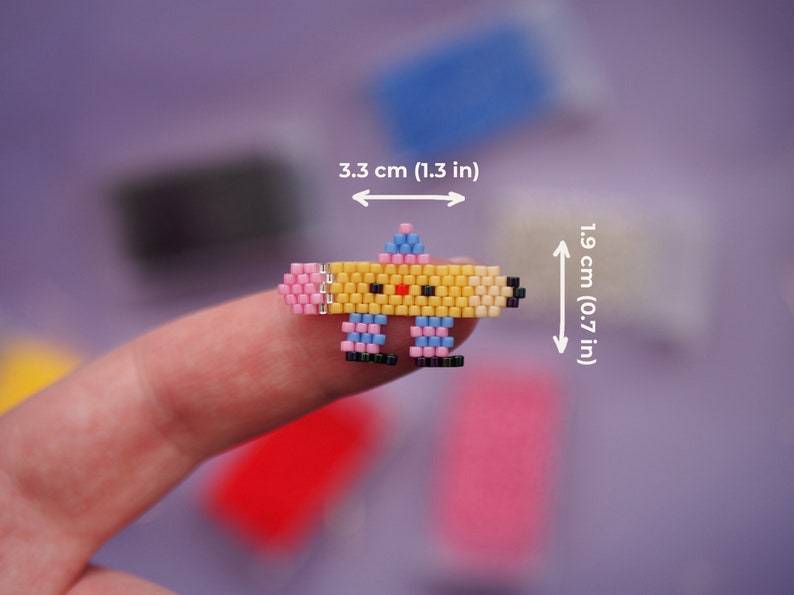 May include: A yellow, pink, and blue beaded pencil charm with a smiling face. The charm is 1.9 inches tall and 3.3 inches wide.