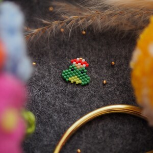 May include: A small green Christmas tree made of beads with a red star on top. The tree is sitting on a dark gray surface.