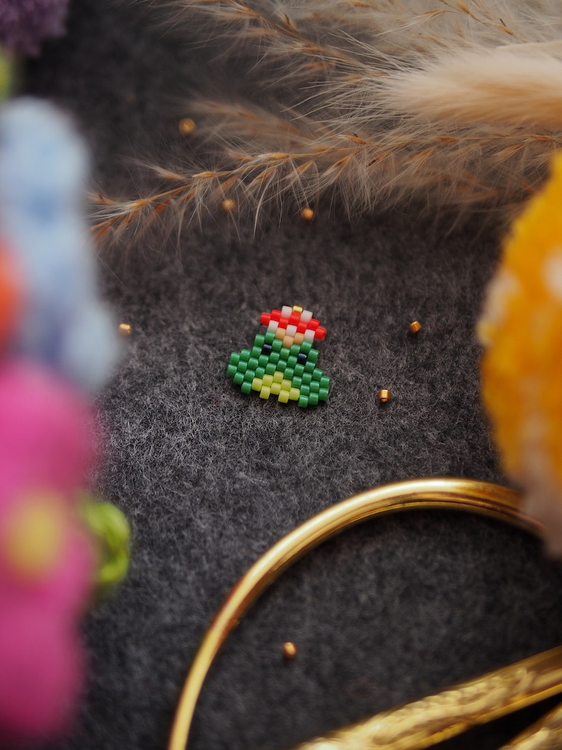 May include: A small green Christmas tree made of beads with a red star on top. The tree is sitting on a dark gray surface.