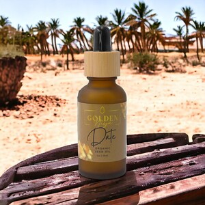 Op de afbeelding: Een bruine glazen fles met een bamboe deksel en een druppelaar. De fles is gelabeld met "Golden Vega Date Organic Seed Oil 1 fl oz | 30ml".