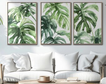 Könnte beinhalten: Drei gerahmte Aquarellbilder von grünen tropischen Blättern, die an einer weißen Wand über einem weißen Sofa mit weißen Kissen hängen. Das Sofa steht in einem Wohnzimmer mit einem Holz-Couchtisch und zwei Holzstühlen.