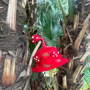 May include: A red felt mushroom hat with white felt dots. The hat is hanging on a tree trunk.
