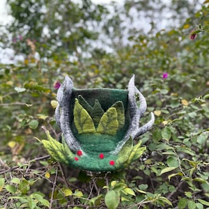 May include: A green felt hat with antlers and leaves, decorated with red berries. The hat is handmade and has a unique, whimsical design.