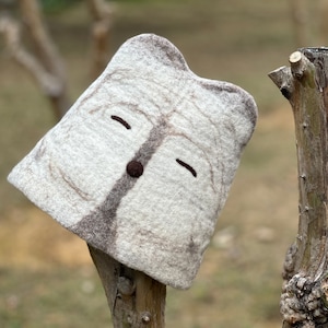 May include: A white felt hat with a brown felt design resembling a face. The hat has two brown eyes and a brown nose.