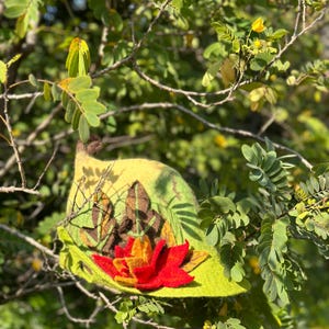 May include: A green and yellow felt hat with a red and orange flower design. The hat is decorated with brown felt leaves.