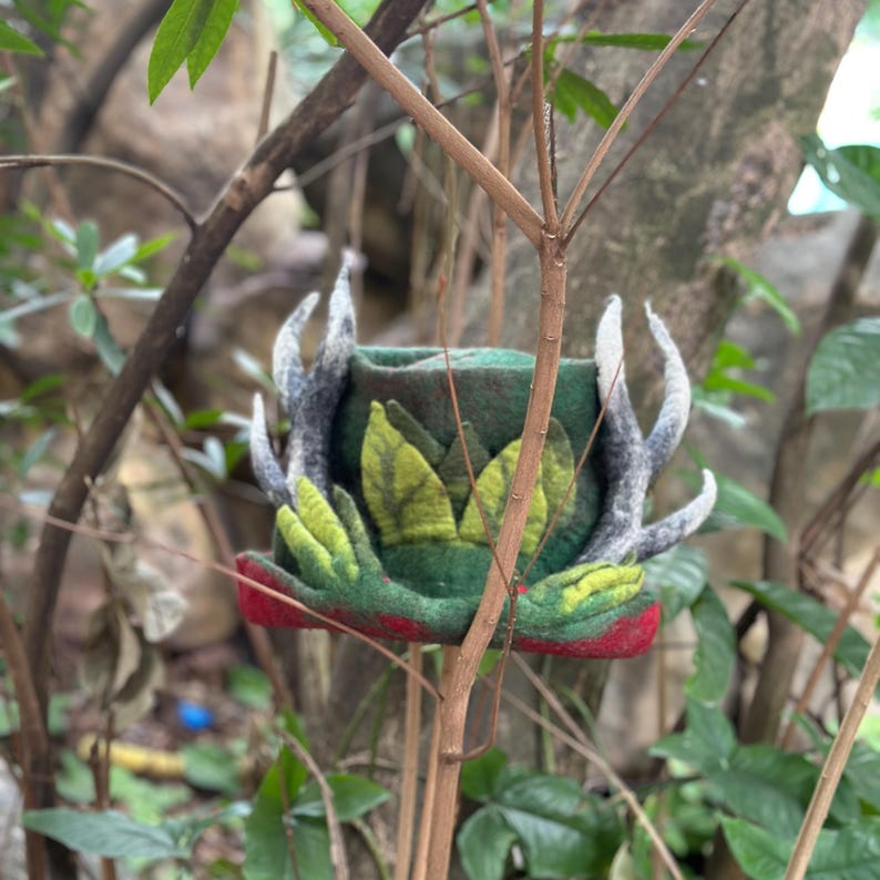 May include: A green felt hat with a red brim and white antlers. The hat is decorated with green felt leaves.