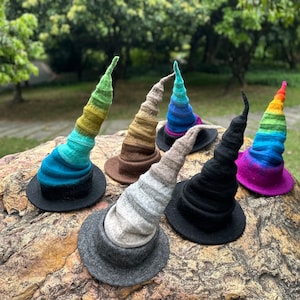 May include: A collection of six felted hats with tall, pointed, spiraling crowns and wide brims. The hats feature various color schemes including solid black, grey, brown, and multi-colored gradients in blue, green, and rainbow patterns.