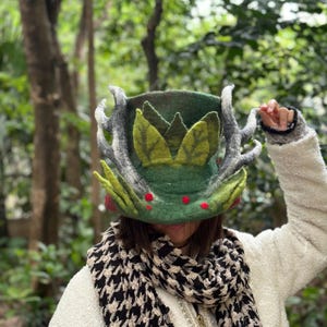 May include: A green felt hat with a large, leafy design and antlers. The hat is decorated with red berries and has a green felt brim.