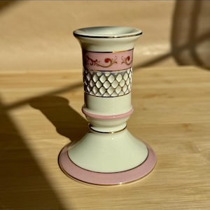 Könnte beinhalten: Ein Vintage-Kerzenhalter aus Porzellan mit cremefarbenem Sockel, akzentuiert mit rosa und goldenen Verzierungen. Der Mittelteil weist ein Rautenmuster und ein rosa Blumendesign auf. Ein klassisches Stück für die Inneneinrichtung.