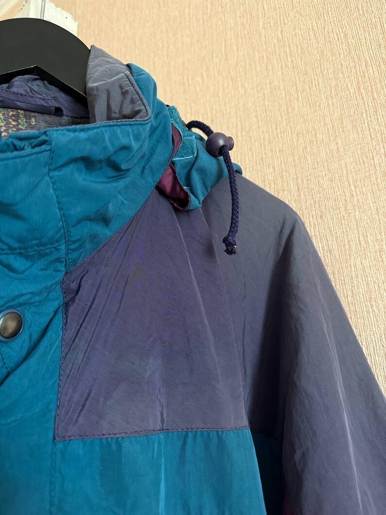 K&ouml;nnte beinhalten: Eine Jacke im Color-Blocking-Design mit Paneelen in Petrol und Dunkelmarineblau. Die Jacke verf&uuml;gt &uuml;ber einen hohen Kragen, eine Kapuze mit dunkelblauem Kordelzug und Stopper sowie einen sichtbaren Metalldruckknopf an der vorderen Knopfleiste.