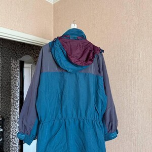 K&ouml;nnte beinhalten: Eine lang&auml;rmelige Jacke mit einem Color-Block-Design in Petrol und Dunkelgrau. Das Kleidungsst&uuml;ck verf&uuml;gt &uuml;ber eine Kapuze mit tiefburgunderrotem Innenfutter, eine Taille mit Kordelzug und verstellbare &Auml;rmelb&uuml;ndchen mit Klettverschl&uuml;ssen.