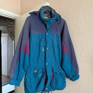 K&ouml;nnte beinhalten: Eine farblich abgesetzte Jacke mit einem t&uuml;rkisfarbenen Hauptteil und dunkelvioletten Eins&auml;tzen an Schultern und &Auml;rmeln. Die Jacke verf&uuml;gt &uuml;ber einen hohen Kragen, eine abnehmbare Kapuze, einen Frontrei&szlig;verschluss mit Druckkn&ouml;pfen und Taschen.