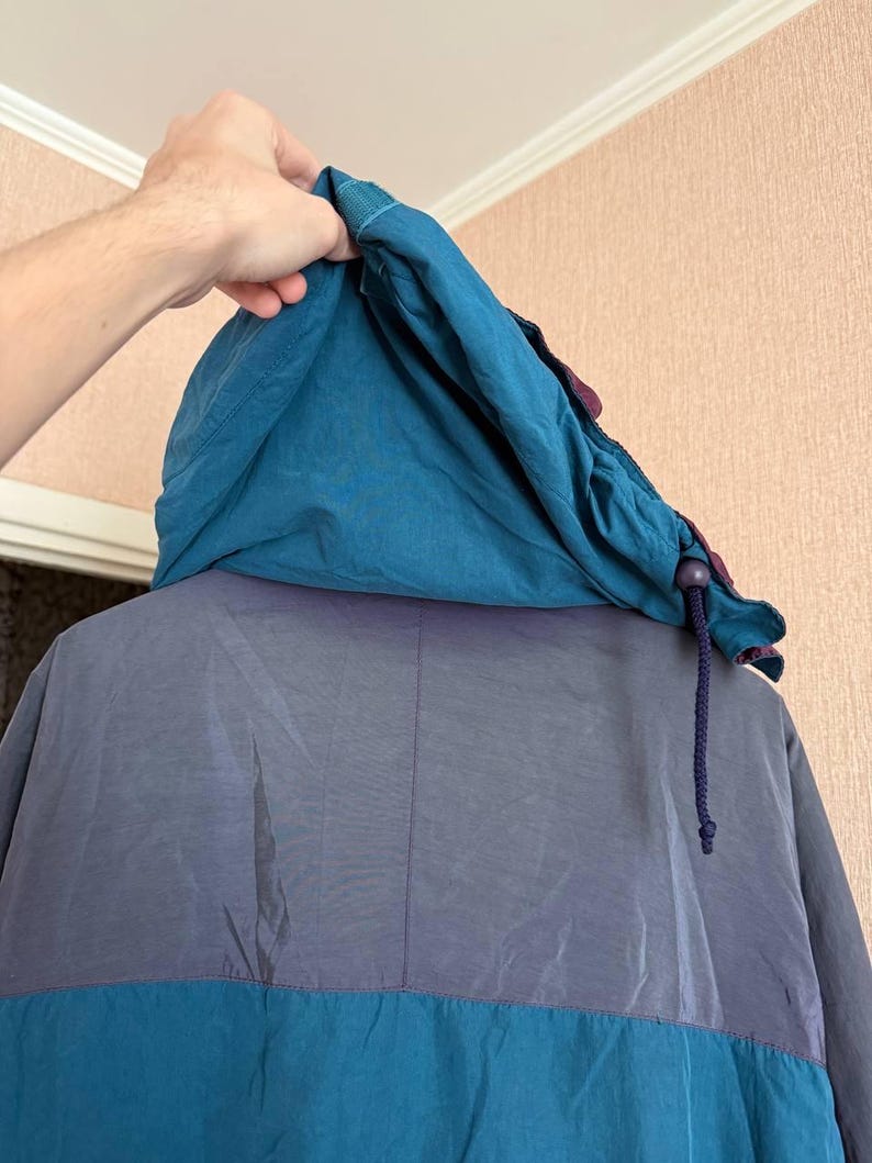 K&ouml;nnte beinhalten: Eine Kapuzenjacke mit Color-Blocking-Design, bestehend aus einer blaugr&uuml;nen Kapuze, einem dunkelgrauen oberen R&uuml;ckenteil und einem blaugr&uuml;nen unteren Bereich. Die Kapuze verf&uuml;gt &uuml;ber einen dunkelblauen Kordelzug mit einem Kunststoff-Stopper.