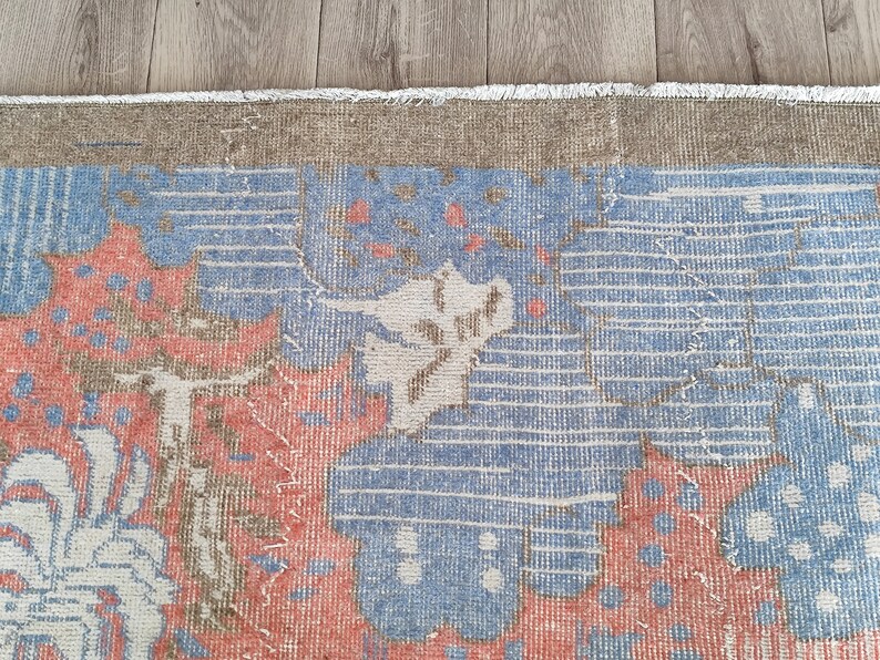 May include: A vintage rug with a blue, pink, and white floral pattern. The rug has a fringe border and is made of wool.