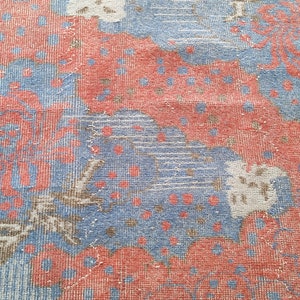 May include: A close-up of a blue and red patterned rug with floral designs. The rug has a textured woven surface.
