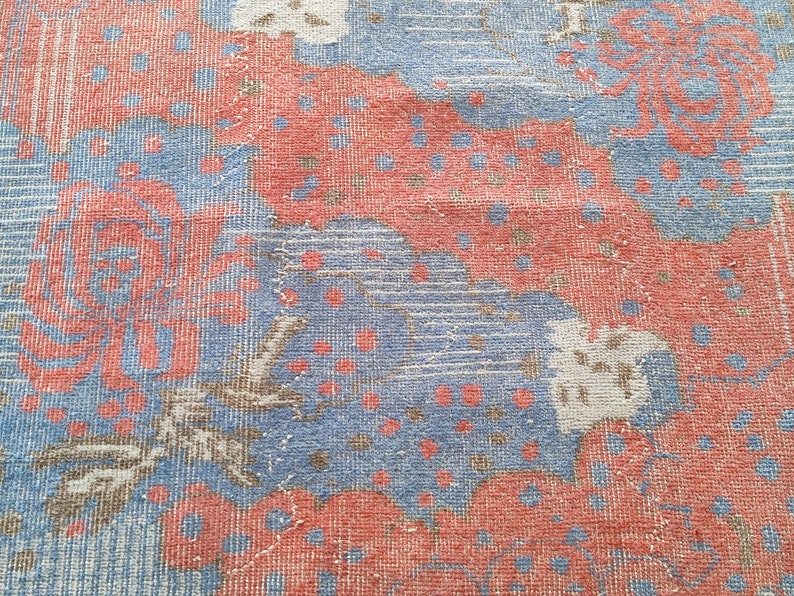 May include: A close-up of a blue and red patterned rug with floral designs. The rug has a textured woven surface.