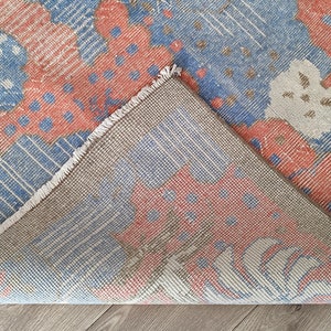 May include: Close-up of the back side of a rug with a blue, red, and white geometric pattern. The rug has a fringe border.