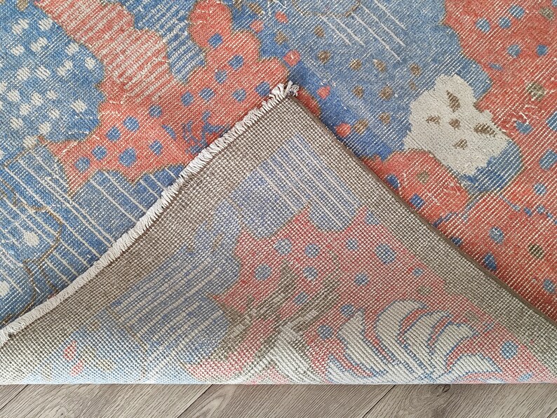 May include: Close-up of the back side of a rug with a blue, red, and white geometric pattern. The rug has a fringe border.