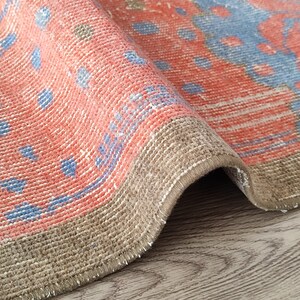 May include: Close-up of a pink and blue patterned rug with a brown fringe. The rug is folded in half and the fringe is visible on the bottom edge.