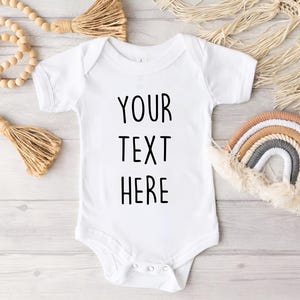 May include: White baby onesie with black text that reads "YOUR TEXT HERE".