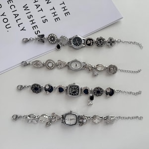 Puede incluir: Cuatro pulseras de plata con dijes con esferas de reloj y dijes decorativos. Las esferas de los relojes tienen formas redondas, cuadradas y rectangulares. Los dijes incluyen flores, lunas y otros elementos decorativos. Las pulseras están sobre una superficie blanca.