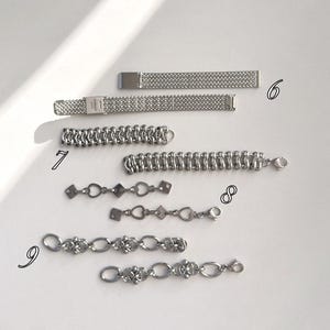 May include: A collection of silver-toned bracelets and chain links. The bracelets feature various designs, including mesh, linked chain, and decorative links with heart and diamond shapes. The pieces are displayed on a white surface.