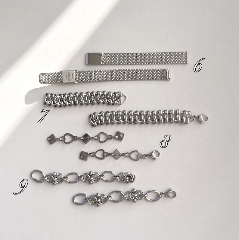 May include: A collection of silver-toned bracelets and chain links. The bracelets feature various designs, including mesh, linked chain, and decorative links with heart and diamond shapes. The pieces are displayed on a white surface.